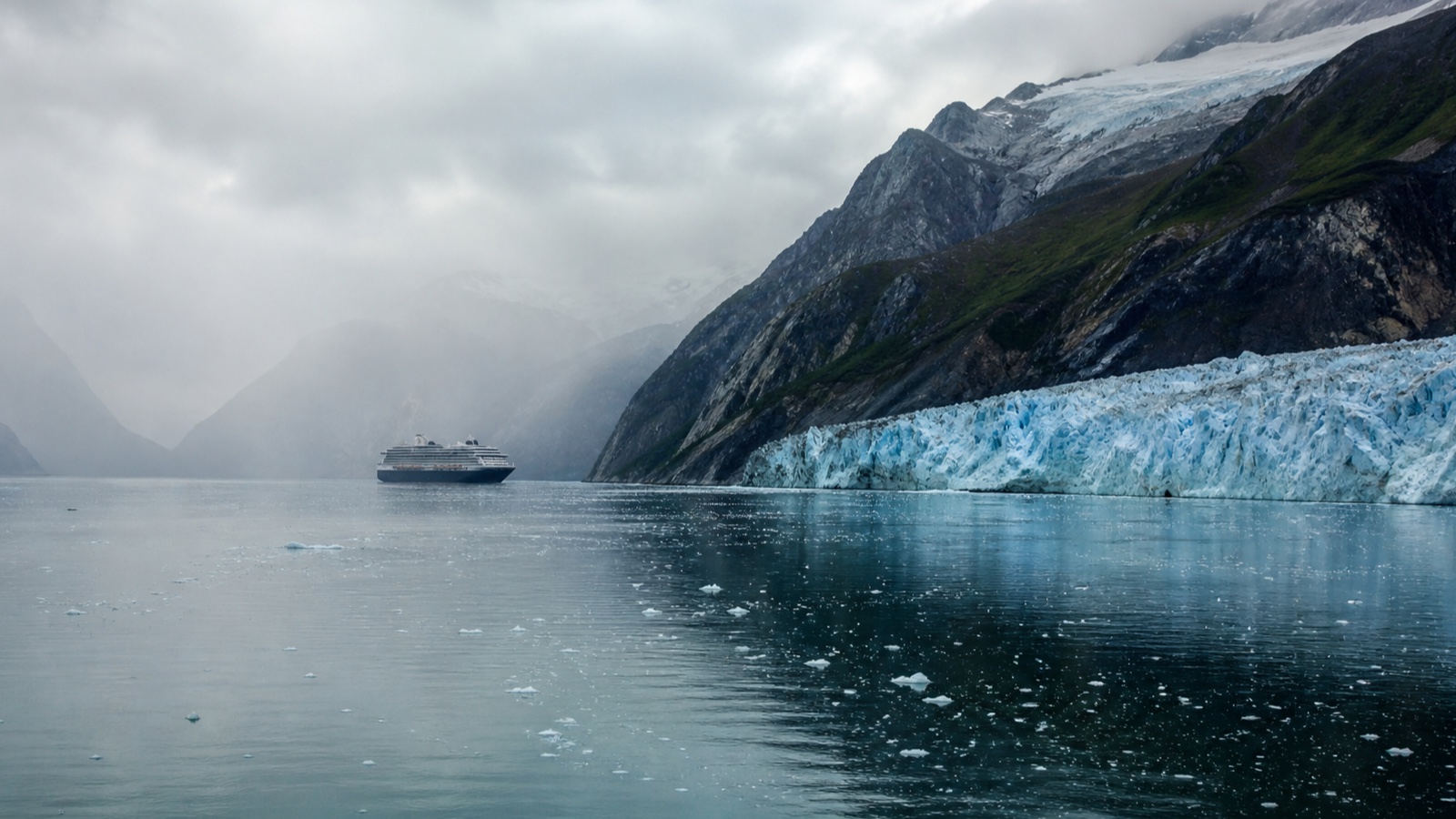 Cruise ship sailing through a broad Alaska glacier passage under natural overcast light