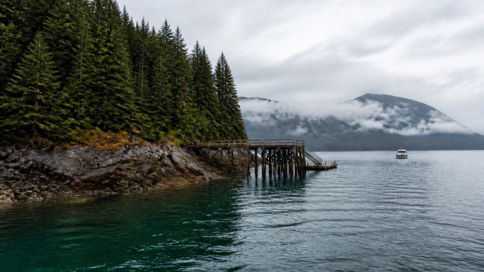 Quiet Icy Strait Point shoreline with evergreen forest and a small excursion boat