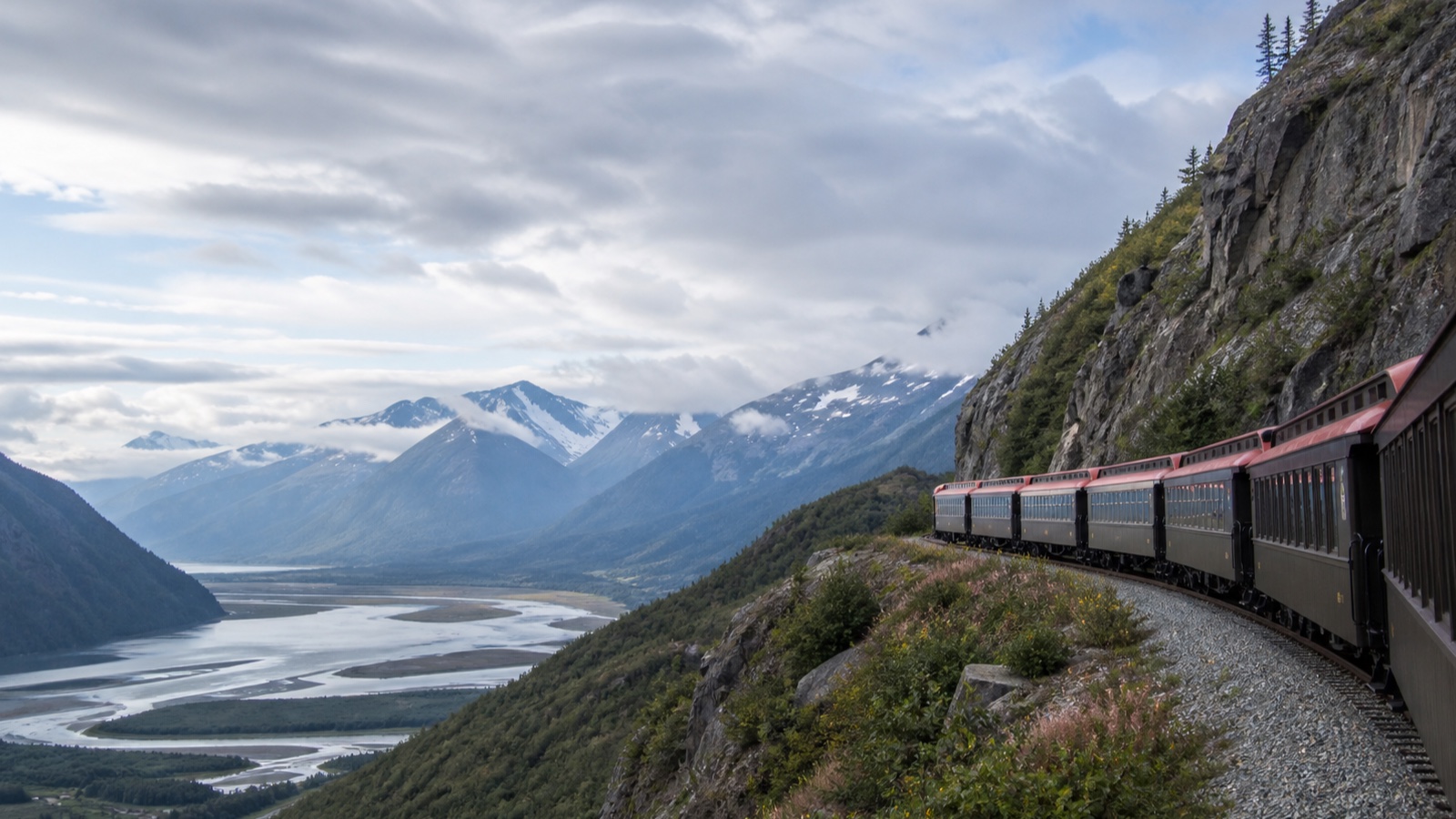 Historic narrow-gauge train crossing a mountain landscape on an Alaska land route