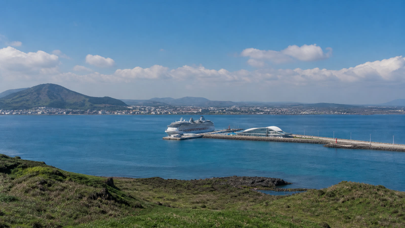 Jeju cruise harbor with an unbranded ship, volcanic coastline and low-rise terminal