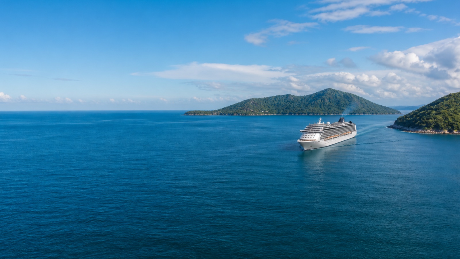 Cruise ship crossing clear Caribbean water between green tropical islands