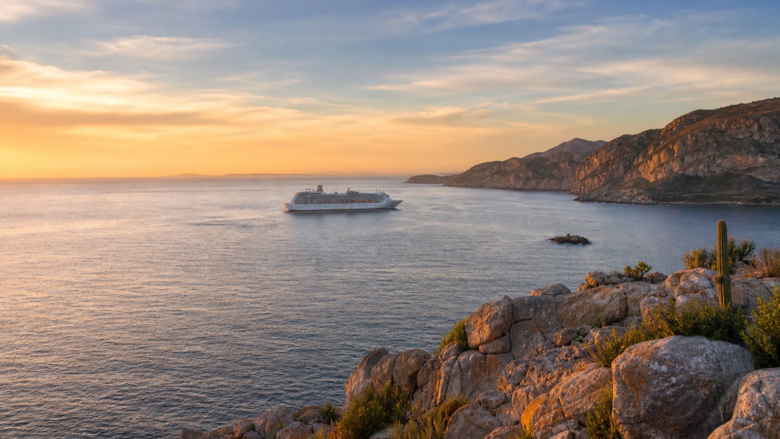 Unbranded cruise ship crossing a rocky Pacific coastline in transitional seasonal light