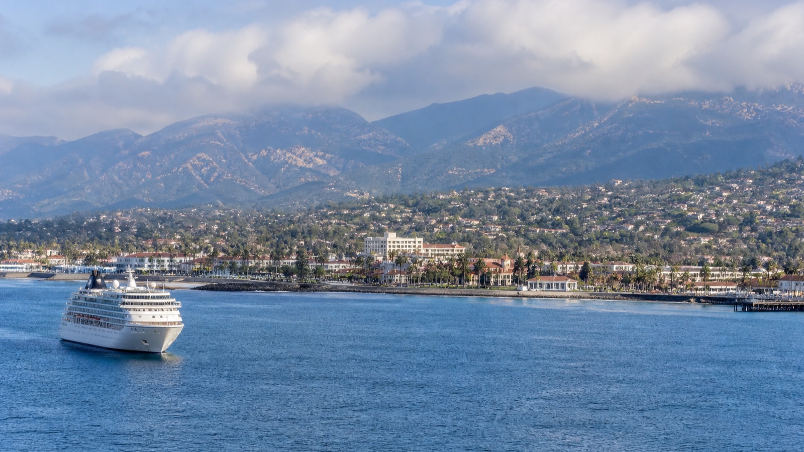 Unbranded cruise ship approaching a California coastal city beneath a marine layer