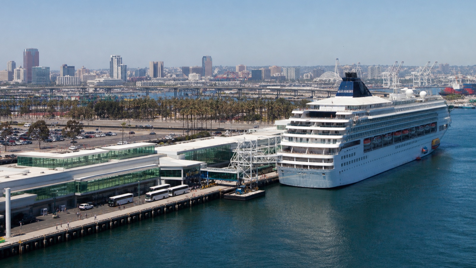 Full-size unbranded cruise ship beside a Southern California terminal and correctly scaled city skyline