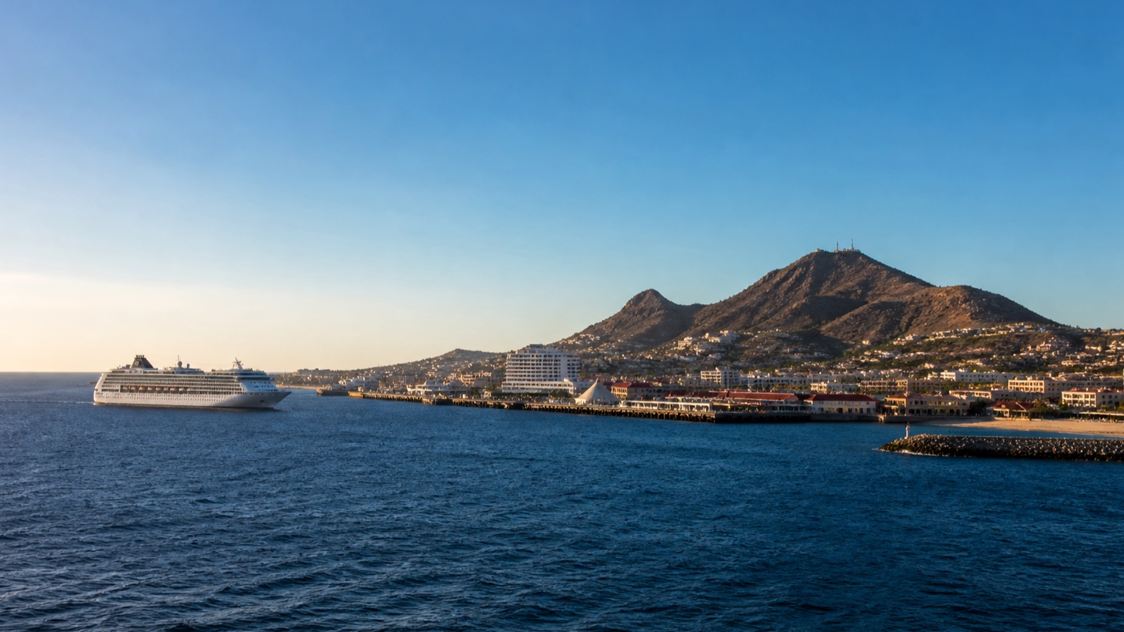Unbranded cruise ship sailing off the Pacific coast with a realistically scaled harbor and coastal city