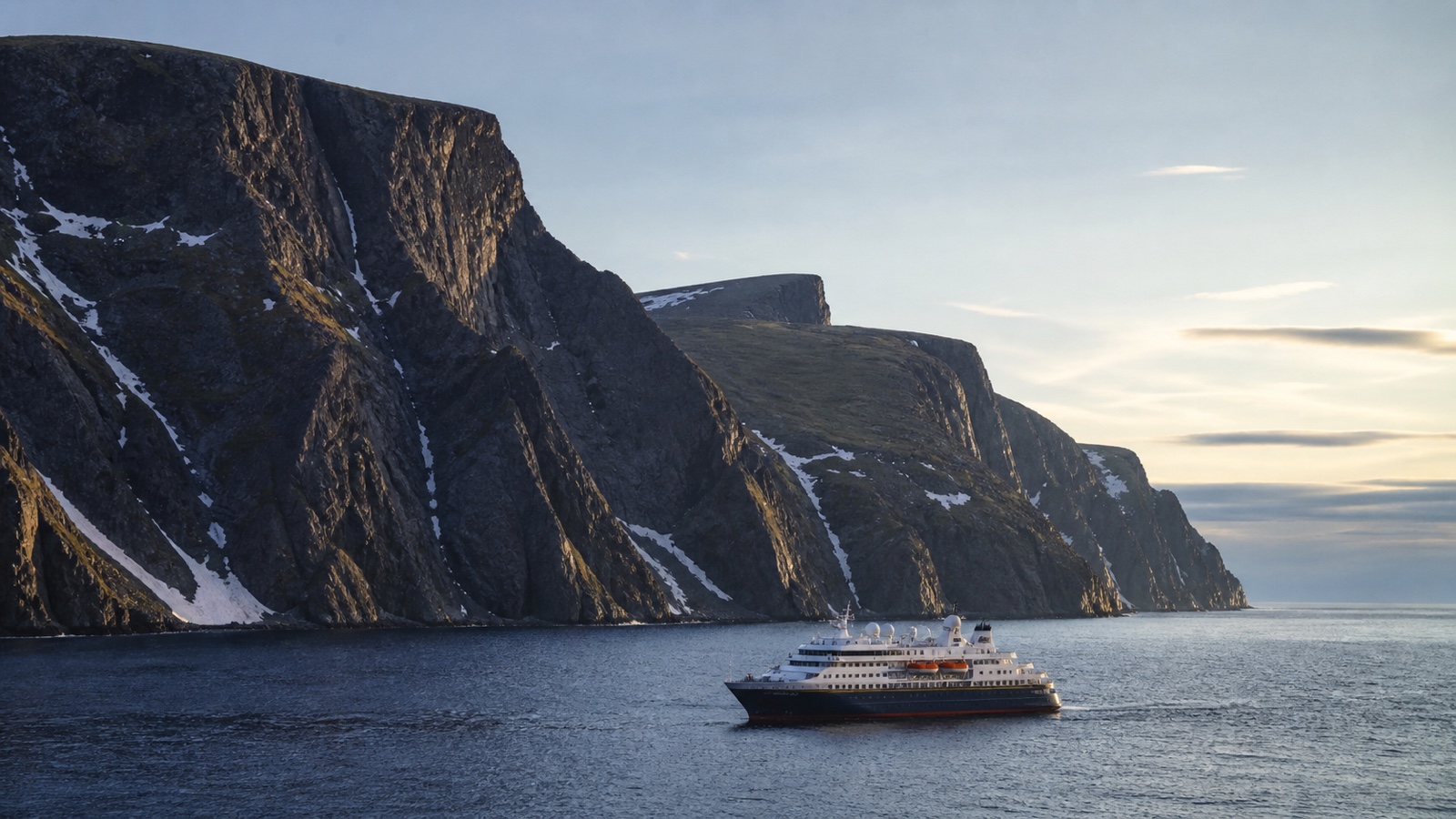 Unbranded cruise ship sailing beneath high Arctic Norway cliffs