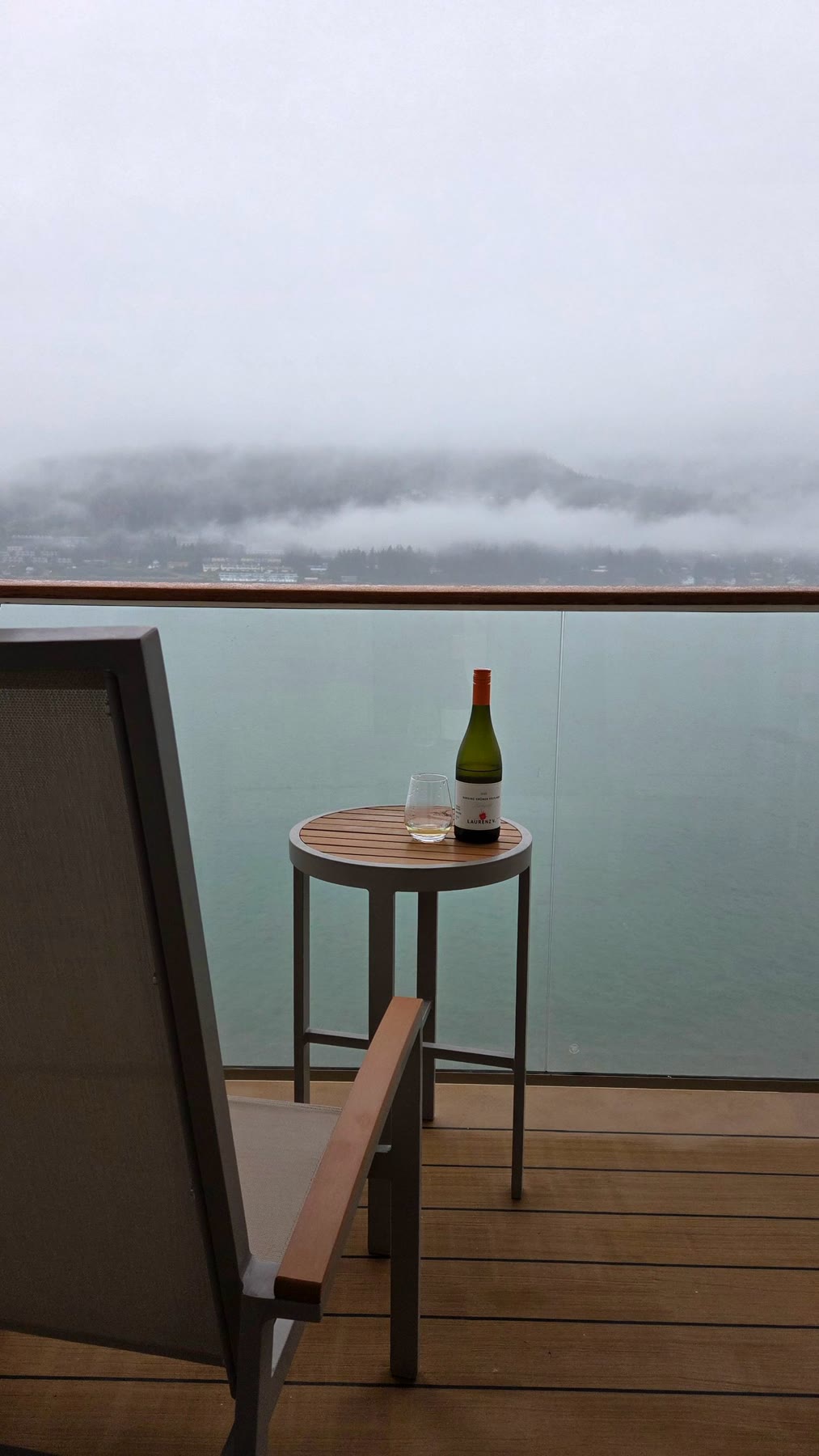 Chair, small table and wine on a private balcony facing a misty Alaska shoreline
