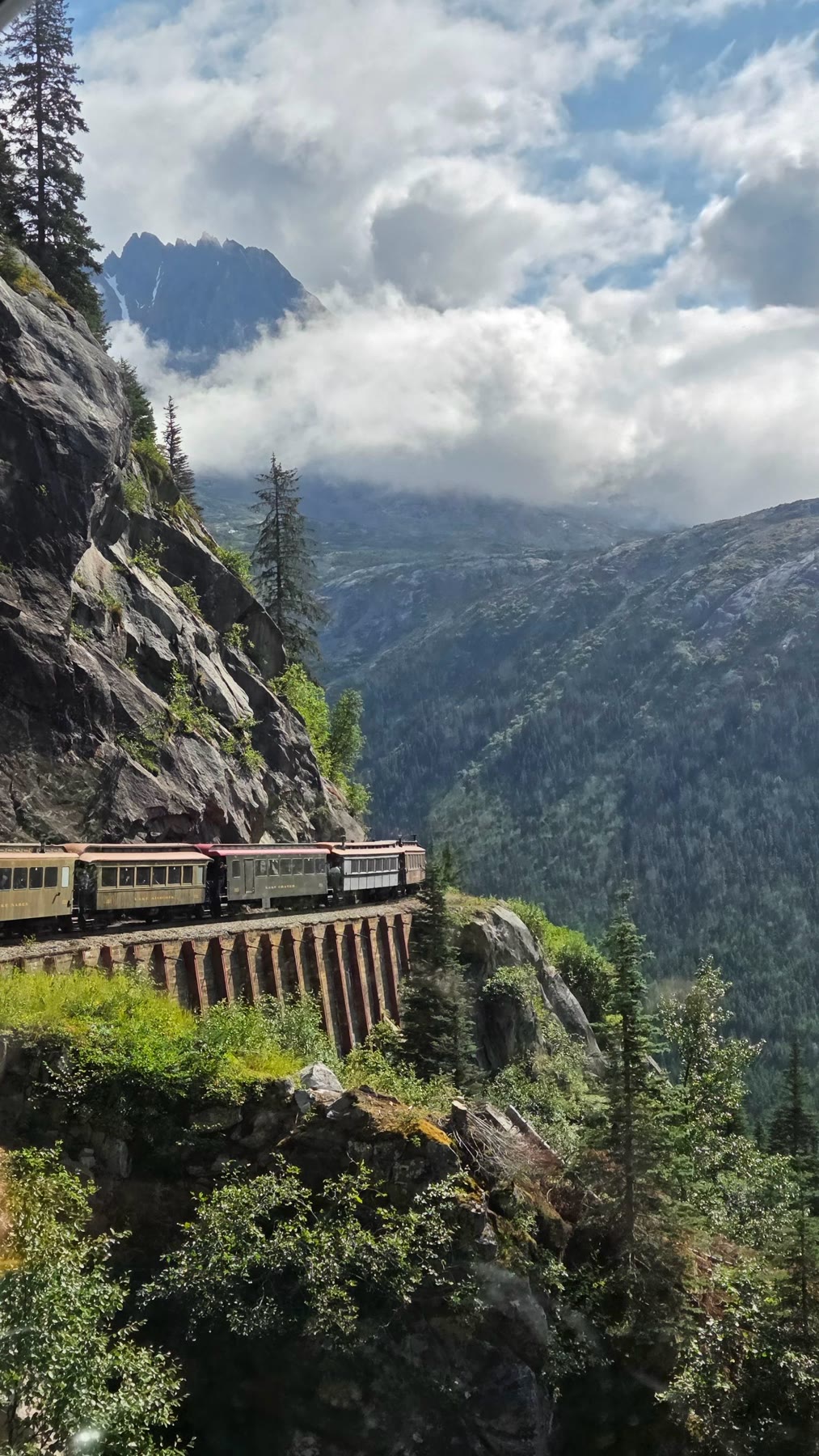 White Pass train rounding a steep mountainside beneath broken cloud